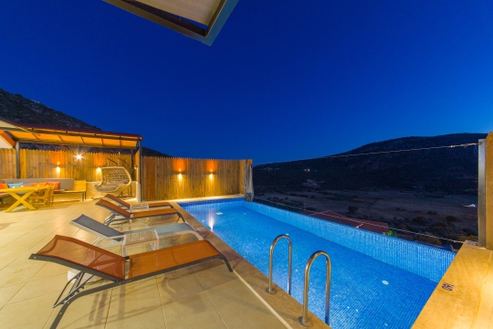 Villa Sidney 1’in gece aydınlatmalı özel yüzme havuzu, havuz başı dinlenme alanı ve etkileyici dağ manzarası.