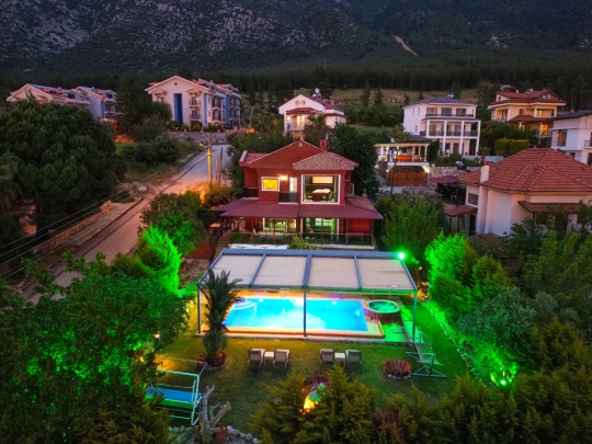 Akşam ışıklarıyla dikkat çeken Villa Heves 1’in özel havuzu, geniş bahçesi ve huzurlu atmosferini yansıtan dış mekan görünümü.