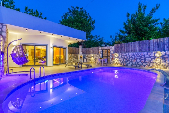 Akşam ışıklarıyla görsel bir şölen sunan özel yüzme havuzu ve modern villa tasarımı. Villa Serter 2’de konforlu ve romantik bir tatil sizi bekliyor.