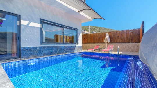 Villa Sidney 4’ün akşam aydınlatmalarıyla öne çıkan korunaklı özel yüzme havuzu ve modern villa dış cephesi.