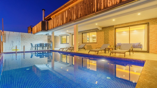 Kalkan Villa Sidney 3’ün modern mimarisi, özel yüzme havuzu ve havuz başı dinlenme alanının akşam görünümü.