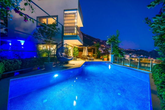 Villa Melissa Duo'nun akşam ışıklandırmalı özel yüzme havuzu ve deniz manzaralı lüks bahçesi.