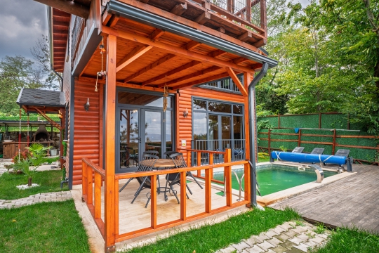 Ahşap çatı kaplamalı veranda altında dış mekân yemek masası, sandalyeler ve hemen yanında yer alan ısıtmalı havuz.
