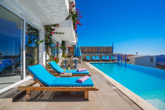 Kalkan Villa Bonny 1’in deniz manzaralı sonsuzluk havuzu, şezlongları ve konforlu havuz başı dinlenme alanı.