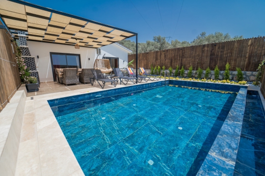 Modern villa mimarisi önünde bulunan özel havuz, geniş teras ve oturma alanı ile huzurlu bir tatil deneyimi sunuyor.