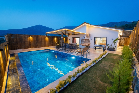 Akşam ışıkları altında aydınlatılan özel yüzme havuzu ve modern villa terası, romantik ve sakin bir atmosfer oluşturuyor.