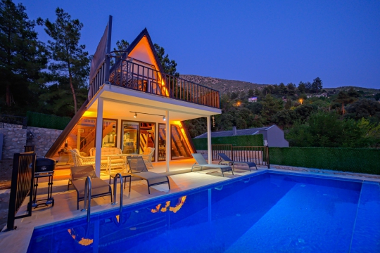 Kalkan Villa Mino Duo'nun ışıklandırılmış modern mimarisi ve özel havuzuyla lüks bungalov tatili için tasarlanan dış görünümü.