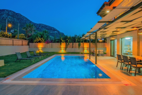 Villa Cozy'nin akşam manzarasında ışıklandırılmış özel yüzme havuzu ve modern yaşam alanları.