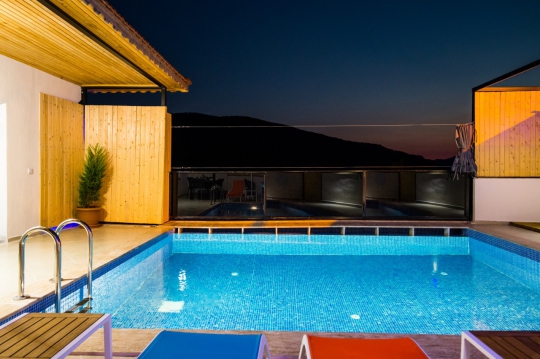 Villa Sidney 2’nin gün batımında ışıklandırılmış özel yüzme havuzu, korunaklı dış alanı ve etkileyici doğa manzarası.
