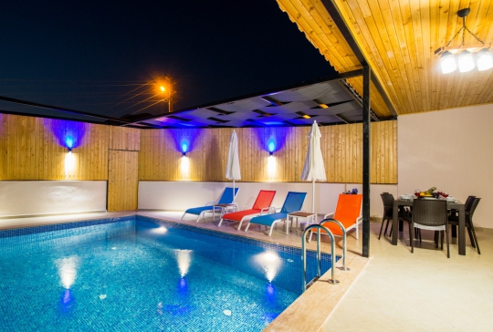 Villa Sidney 2’nin gece aydınlatmalı korunaklı özel yüzme havuzu, şezlongları ve modern havuz başı dinlenme alanı.