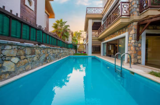 Villa Eleas Duo’nun uzun özel yüzme havuzu ve taş duvarlı dış alanı; Göcek’te korunaklı havuzlu villa tatili için ideal.