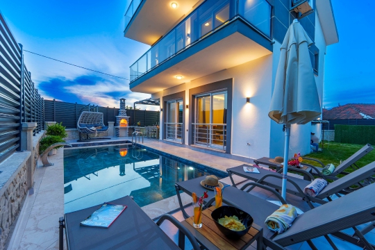 Villa Akros'un korunaklı özel yüzme havuzu ve iki katlı modern mimarisiyle dış cephe görünümü.