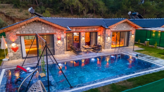 Villa New Star 1'in akşam ışıklandırmalı özel yüzme havuzu ve taş mimarisiyle lüks balayı villası atmosferi.