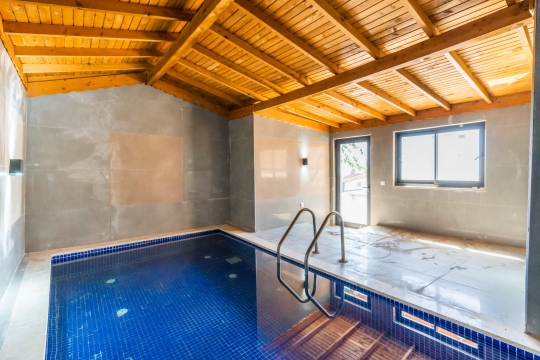 Villa New Porto’nun kapalı yüzme havuzu, ahşap tavan tasarımı ve modern iç mekânıyla dört mevsim konforlu kullanım imkânı sunmaktadır.