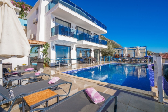 Villa New Porto’nun deniz manzaralı özel sonsuzluk havuzu, şezlong alanları ve modern mimarisiyle geniş dış yaşam alanı.