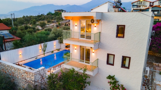 Işıklandırılmış taş dış cephesi ve mavi aydınlatmalı yüzme havuzuyla Villa Romance'ın akşam atmosferi.