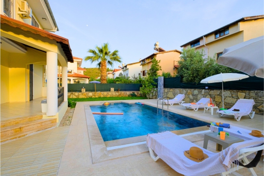 Fethiye Villa Beta’nın korunaklı özel yüzme havuzu, şezlonglu güneşlenme alanı ve palmiye detaylı bahçe görünümü.