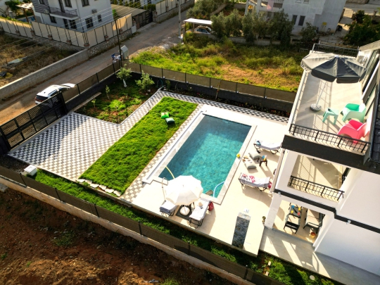 Villa Varoni’nin özel yüzme havuzu, geniş çim bahçesi ve güneşlenme alanlarının üstten genel görünümü.
