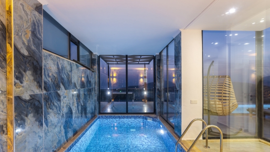 Villa Boho 1’in kapalı yüzme havuzu, modern taş duvar detayları ve ısıtma seçeneğiyle yılın farklı dönemlerinde konforlu kullanım imkânı sağlamaktadır.