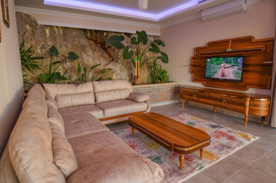 Doğal taş detaylı duvar, konforlu köşe koltuk takımı ve ahşap sehpa içeren lüks salon alanı.