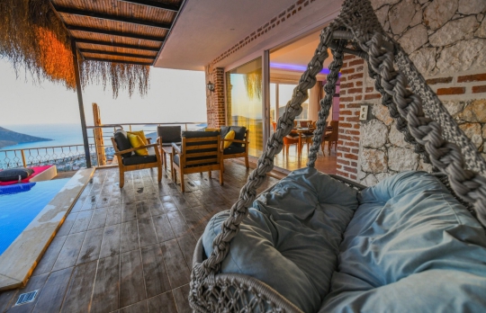 Ahşap kaplama verandada yer alan konforlu bahçe salıncağı, dış mekân oturma grubu ve panoramik kalkan manzarası.