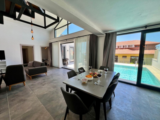 Villa Kresivaya Duo 2'nin yüksek tavanlı açık plan mutfağı, yemek alanı ve havuz manzaralı ferah yaşam alanı.