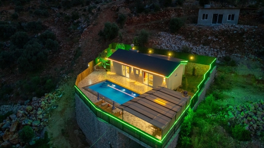 Seydikemer Saklıkent'te konumlanan Villa Roze'nin özel havuzu ve ışıklandırılmış bahçesinin havadan gece görünümü.