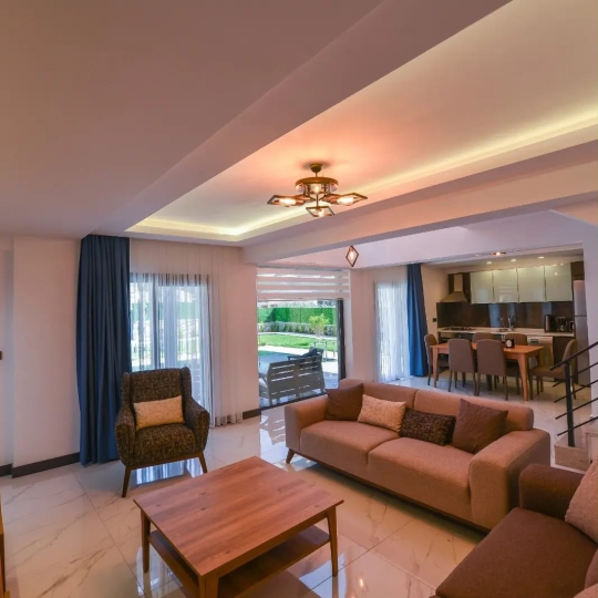 Modern tasarımlı Villa Olea 2’nin ferah salonu, konforlu oturma grubu ve bahçe manzarasıyla keyifli vakit geçirme imkânı sunuyor.