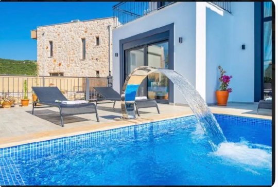 Kaş Villa Melodi’nin özel yüzme havuzu, dekoratif şelale detayı ve modern taş mimarisiyle lüks havuz başı görünümü.