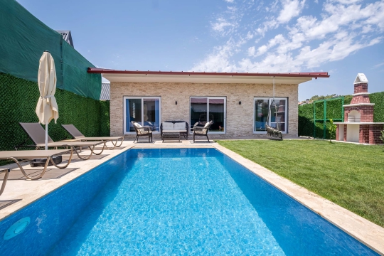 Fethiye Çiftlik Villa Vimo’nun 6 x 3 metre özel yüzme havuzu, taş villa cephesi ve havuz başı güneşlenme alanı.