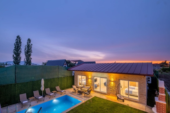 Villa Vimo’nun gün batımında ışıklandırılmış özel havuzu, geniş bahçesi ve tek katlı taş villa mimarisi.