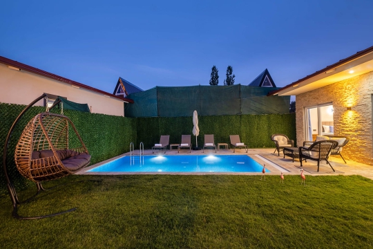 Villa Vimo’nun akşam ışıklandırmalı özel havuzu, şezlongları ve mahremiyet sağlayan çevrili bahçe alanı.