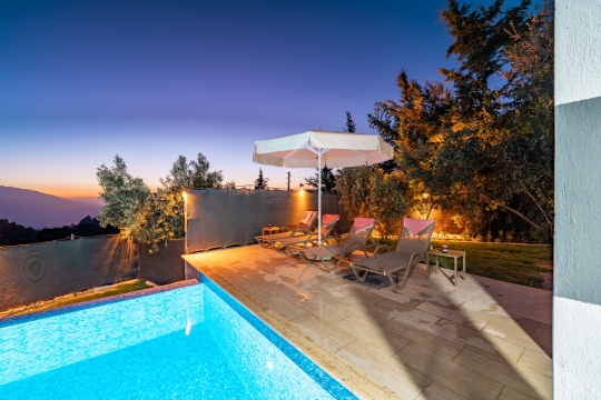 Villa Apilla’nın akşam ışıklandırmalı özel havuzu, şezlonglu güneşlenme alanı ve doğayla iç içe bahçe görünümü.