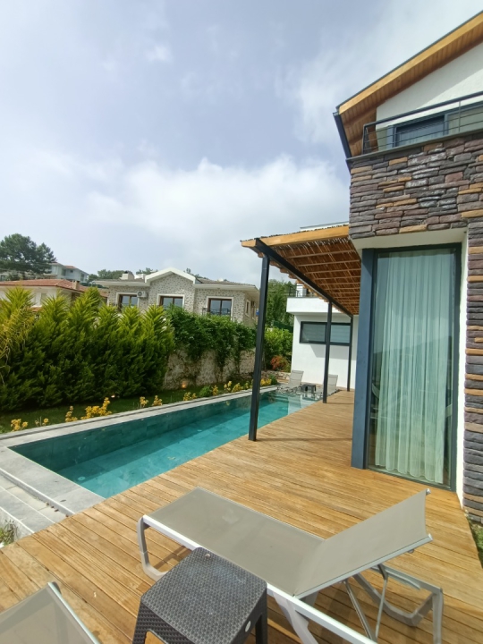 Villa Twins 20’nin 12 metre uzunluğundaki özel yüzme havuzu, ahşap havuz çevresi ve modern dış cephe görünümü.