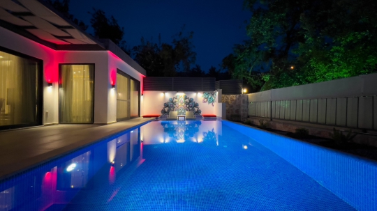 Villa Balies’in gece ışıklandırmalı özel havuzu, modern dış cephesi ve mahremiyet sunan korunaklı bahçe görünümü.