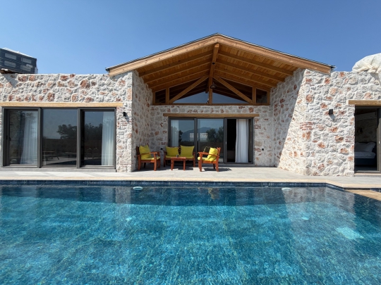 Doğal taş duvarlı villanın özel havuzu ve ahşap detaylı verandası, huzurlu bir tatil için ideal açık yaşam alanı oluşturuyor.