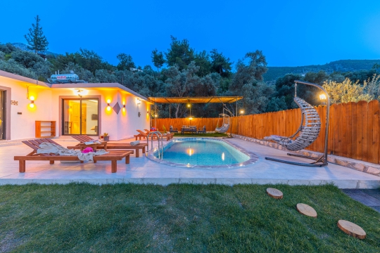 Akşam ışıklandırmasıyla huzurlu atmosfer sunan korunaklı havuzlu villa bahçesi.
