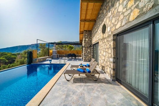 Deniz manzaralı villanın geniş havuz terası, şezlonglar ve şemsiye.