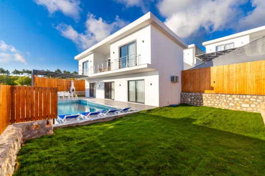 Çim bahçe alanı ve havuz terası bulunan modern iki katlı kiralık villa görünümü.