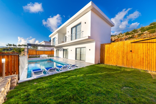 Çim bahçe alanı, şezlong takımları ve yüzme havuzu bulunan modern kiralık villa.