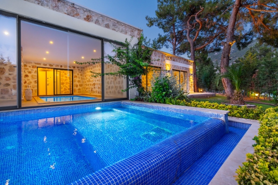 Villa Milenyum 1 korunaklı havuz terası, cam cepheler ve şık akşam aydınlatması.
