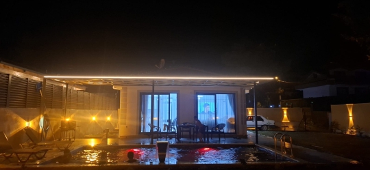 Şerit LED ve spot aydınlatmalarla donatılmış villanın gece veranda ve havuz alanı görünümü.