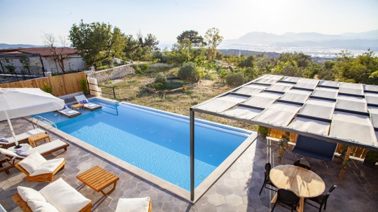 Gölgelikli pergola altından özel yüzme havuzuna, zeytin ağaçlarına ve Patara deniz manzarasına bakan geniş açı.