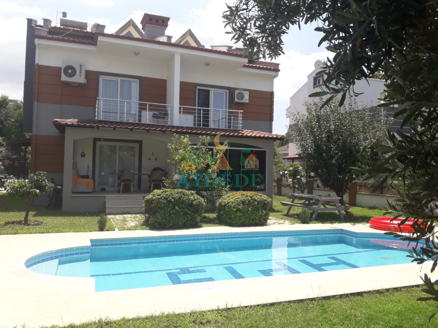 Fethiye Çalış'ta bulunan Villa Cozi'nin özel yüzme havuzu, geniş bahçesi ve modern dış cephesini gösteren görünüm.