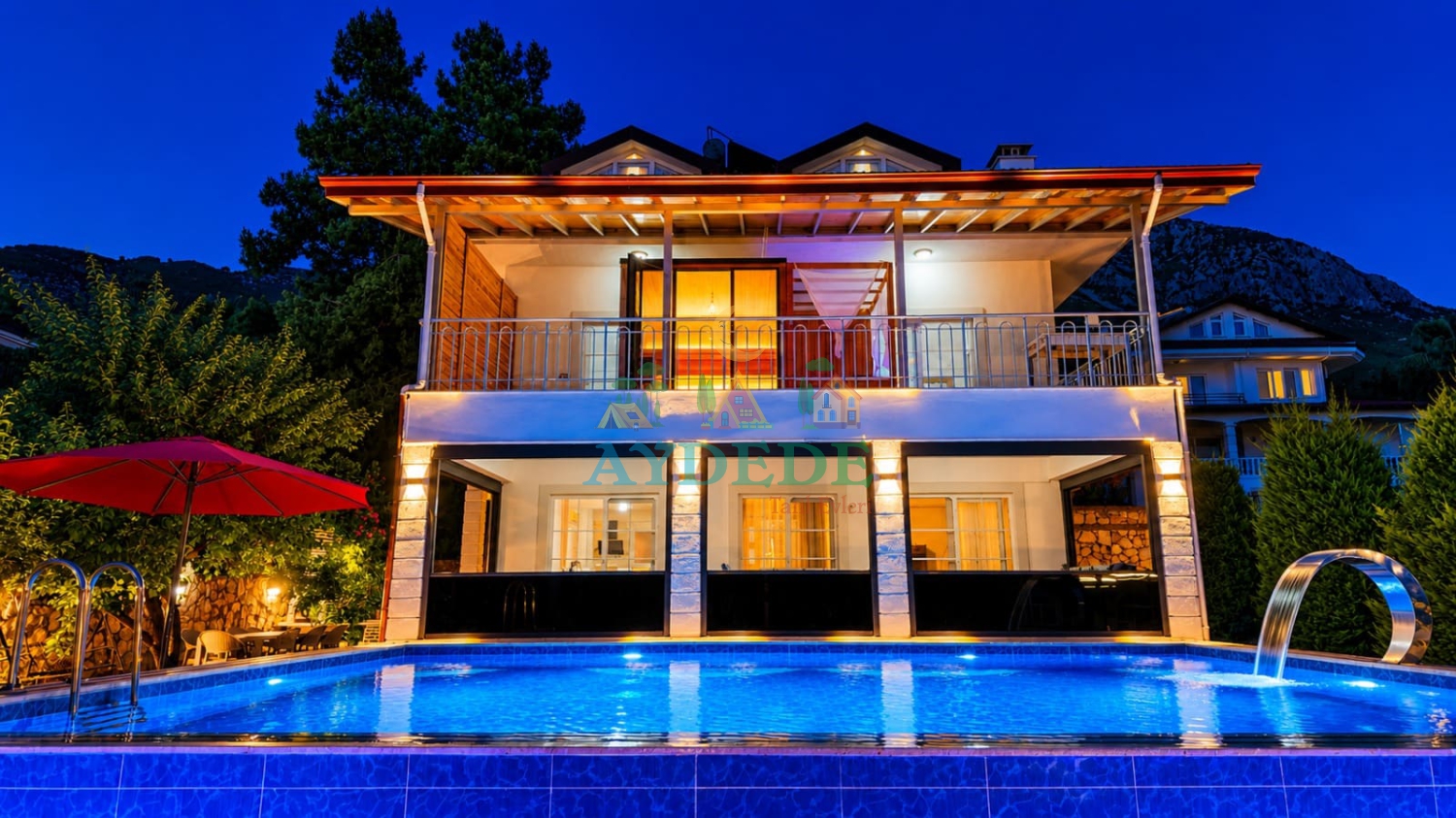 Villa Green'in ışıklandırılmış dış cephesi ve özel yüzme havuzu, Fethiye Yeşil Üzümlü'de lüks tatil deneyimi sunmaktadır.