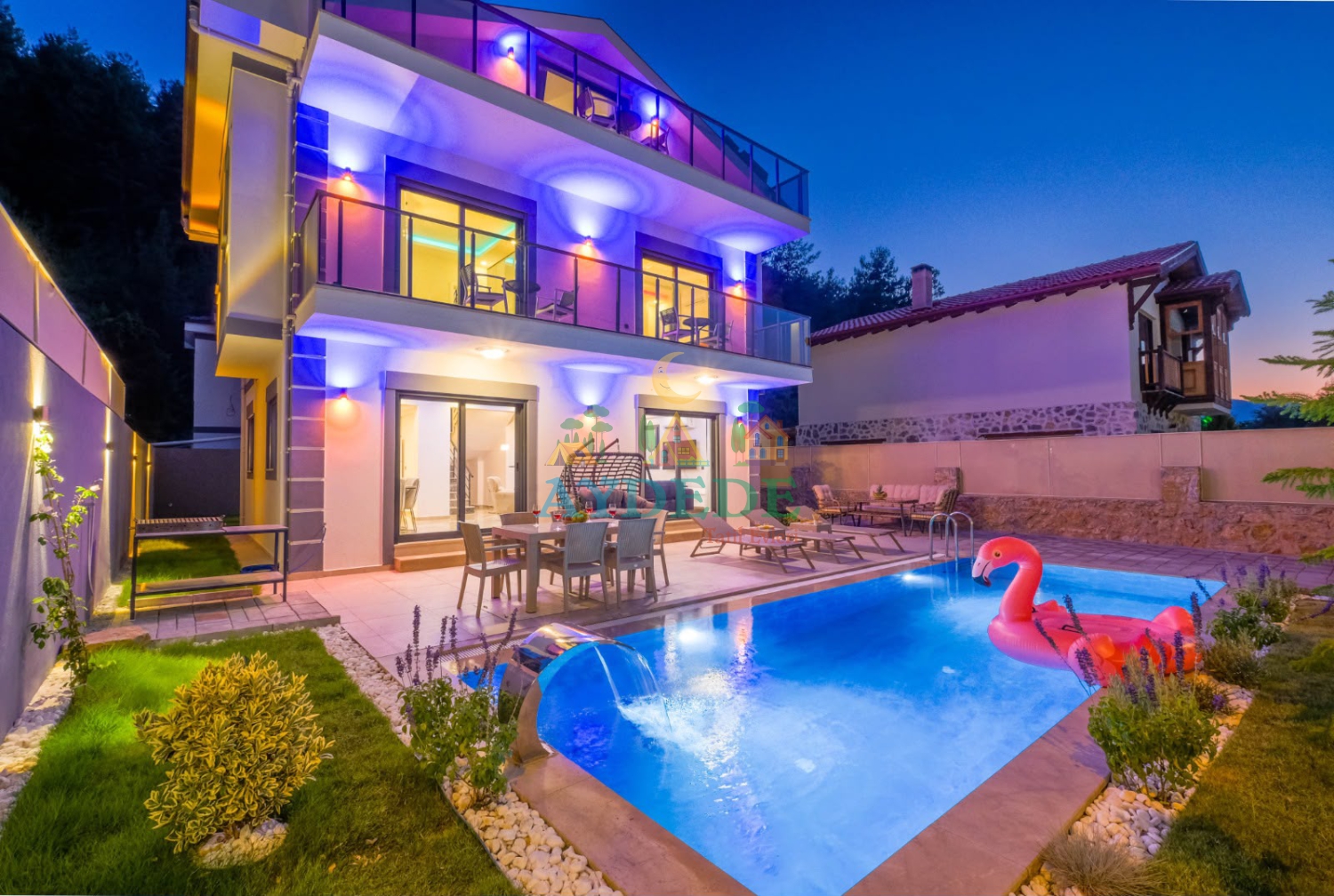Fethiye Yeşilüzümlü'de bulunan Villa Petra'nın özel yüzme havuzu, modern mimarisi ve akşam ışıklandırmasıyla dikkat çeken dış görünümü.