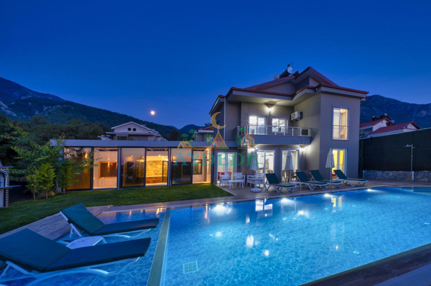 Villa La Sierre 2'nin Fethiye Ovacık Ölüdeniz'de bulunan özel yüzme havuzu, geniş bahçesi ve modern mimarisiyle akşam saatlerinde büyüleyici dış görünümü.