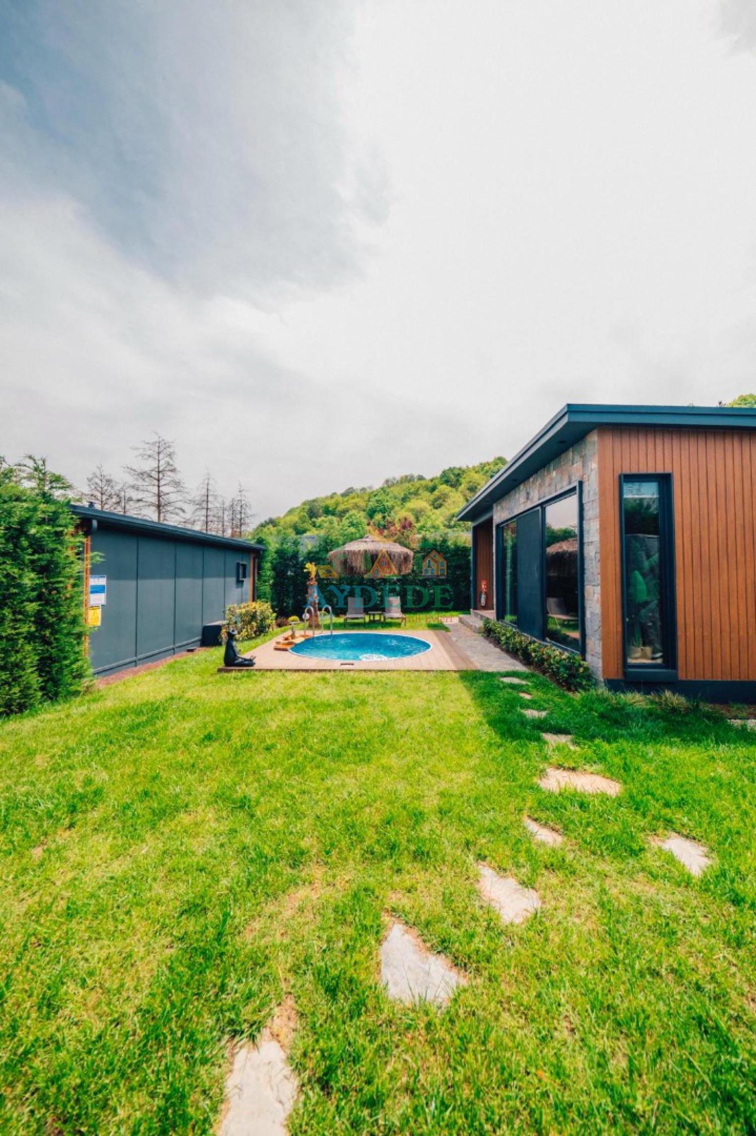 Çim bahçeli, özel dairesel ısıtmalı yüzme havuzlu ve modern mimarili Arven Deluxe bungalov dış cephesi.