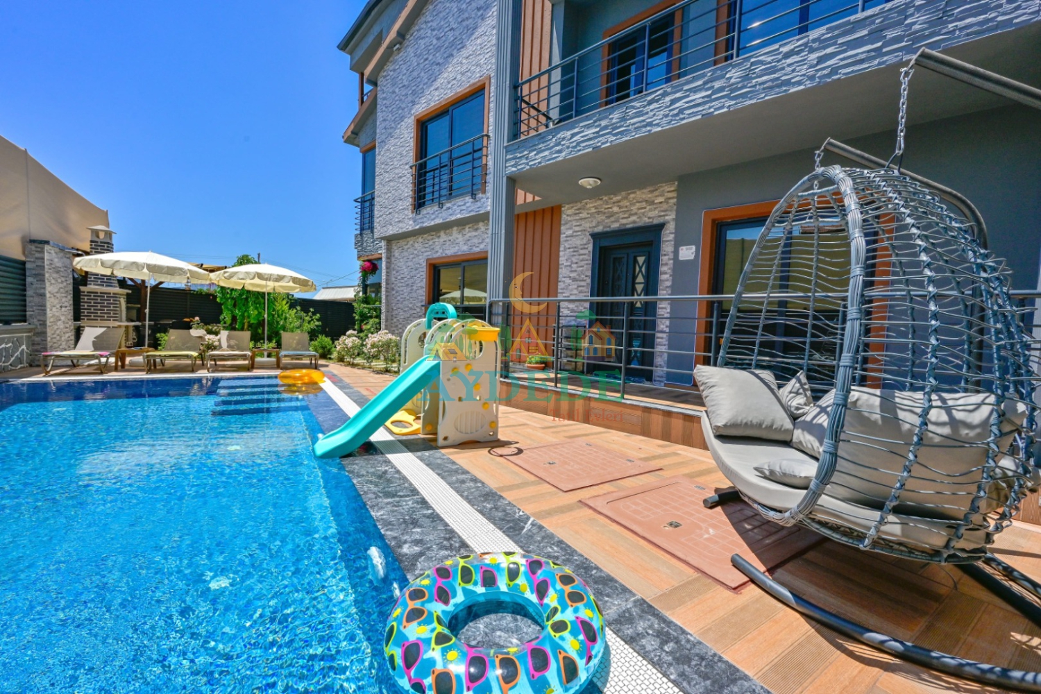 Villa Teadora'nın özel yüzme havuzu ve çocuk kaydıraklı bahçesinden gündüz görünümü.