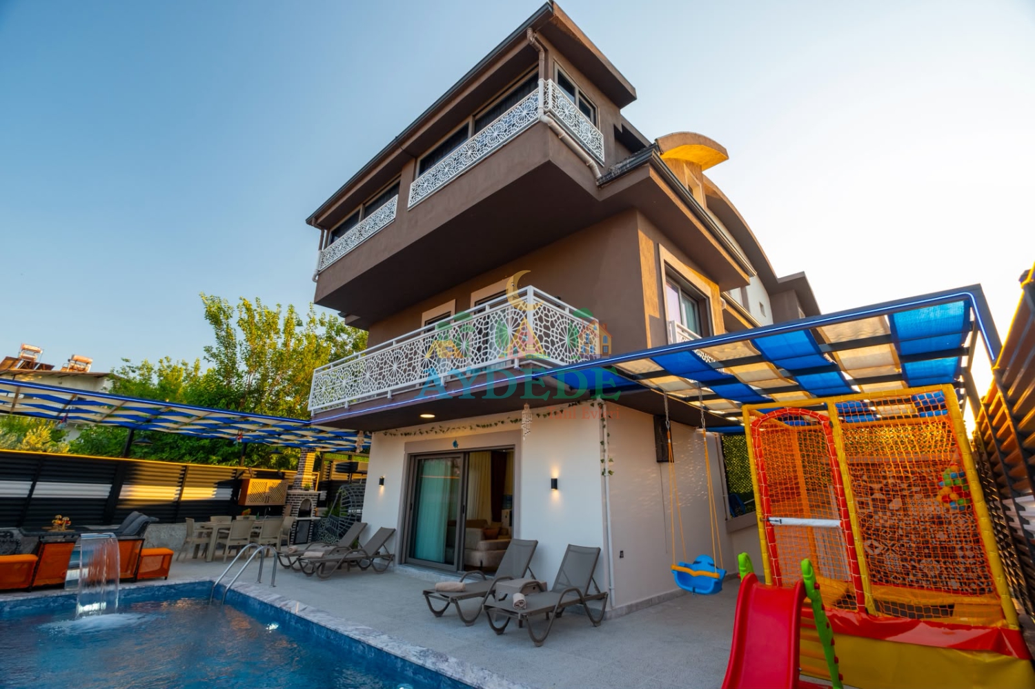 Fethiye Seydikemer'de korunaklı özel yüzme havuzu, çocuk kaydırağı ve oyun alanına sahip 3 katlı lüks Villa Apple'ın gündüz dış cephe görünümü.